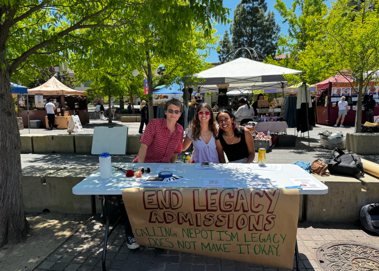 Three students sit behind a table with a banner that reads "End legacy admissions."